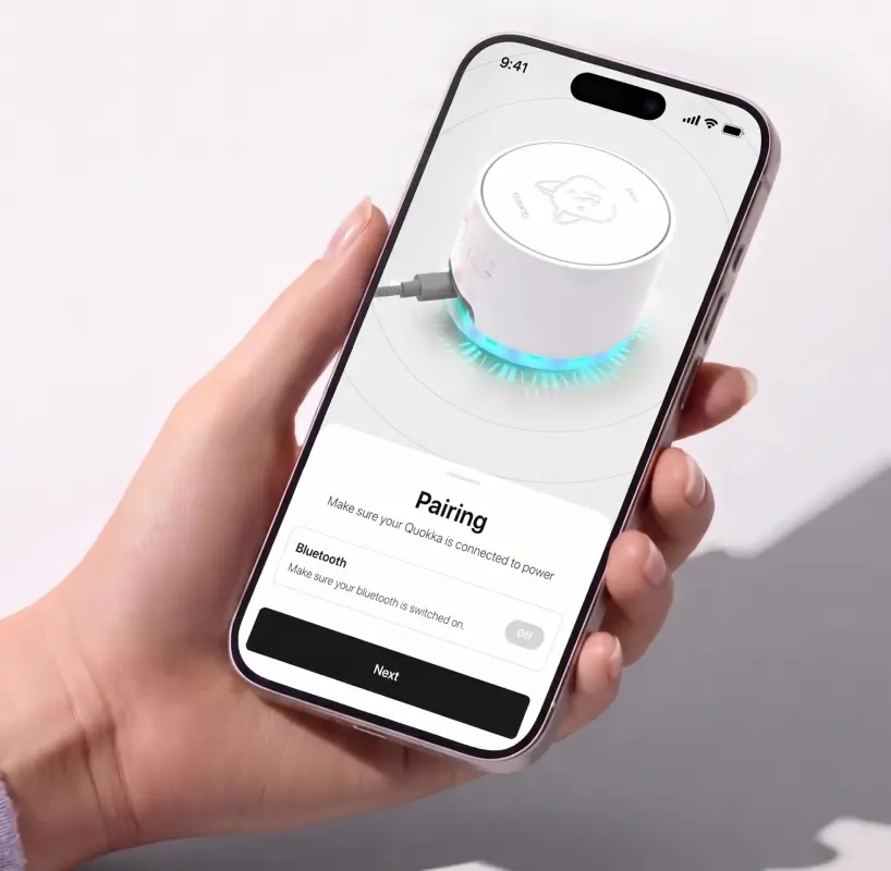 A hand holding a phone pairing with the Quokka device