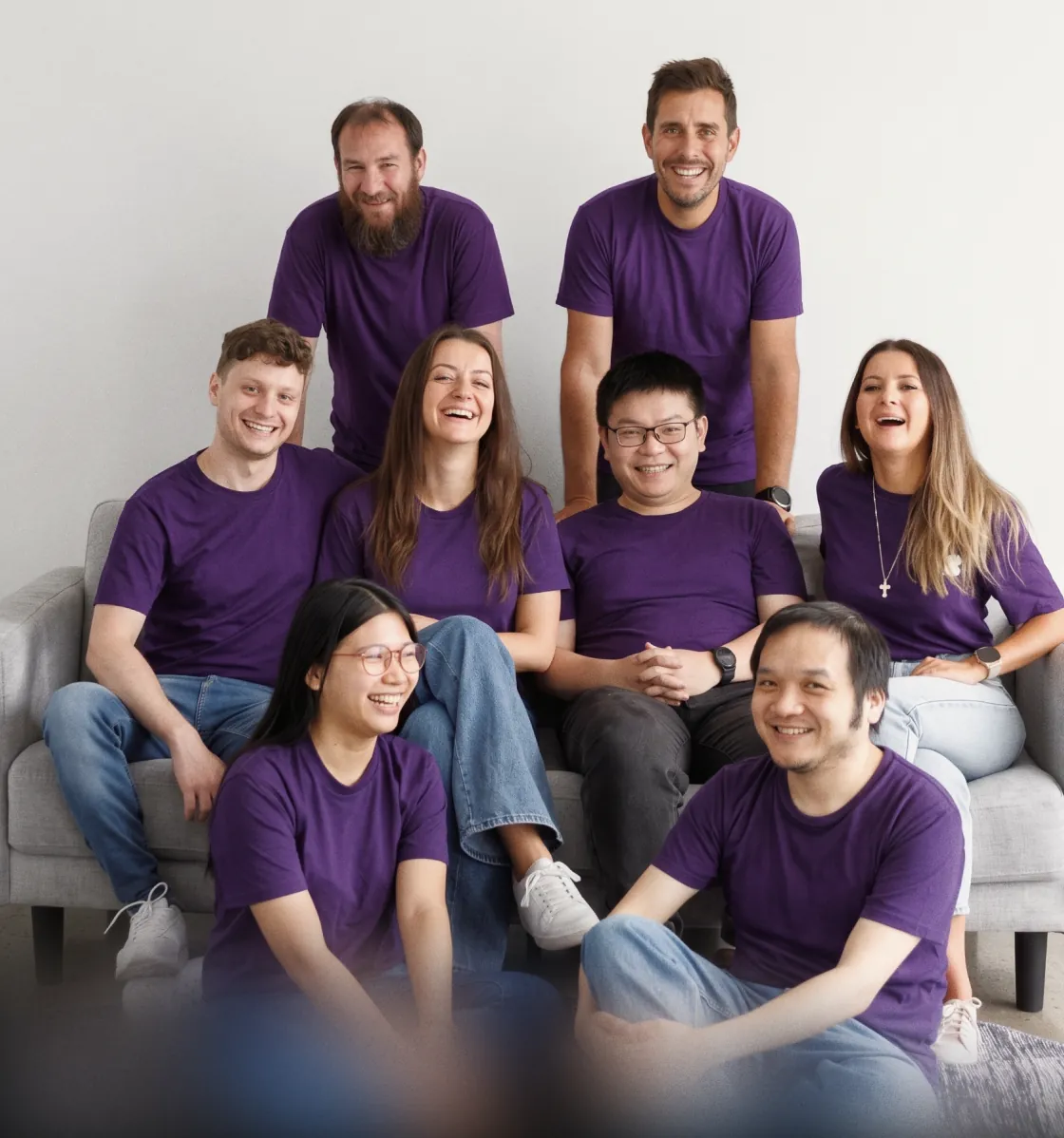 Eight people in matching purple T-shirts laughing together on and around a sofa